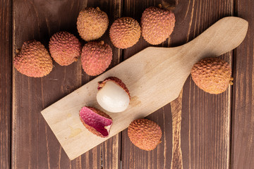 Group of nine whole one piece of fresh lychee on wooden cutting board flatlay on brown wood