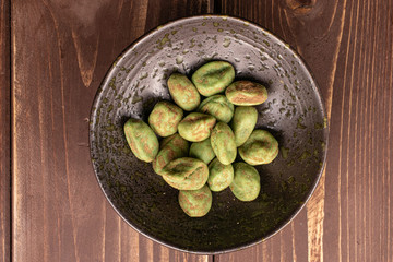 Lot of whole wasabi green peanut in glazed bowl flatlay on brown wood