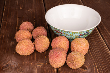 Group of nine whole fresh lychee with blue chinese ceramic bowl on brown wood