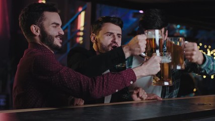 Charismatic good looking smiling large guys cheers with big glasses of beer in a pub they enjoying the time together while drinking at bar table