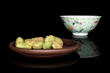 Lot of whole wasabi green peanut with brown ceramic coaster and blue chinese ceramic bowl isolated on black glass