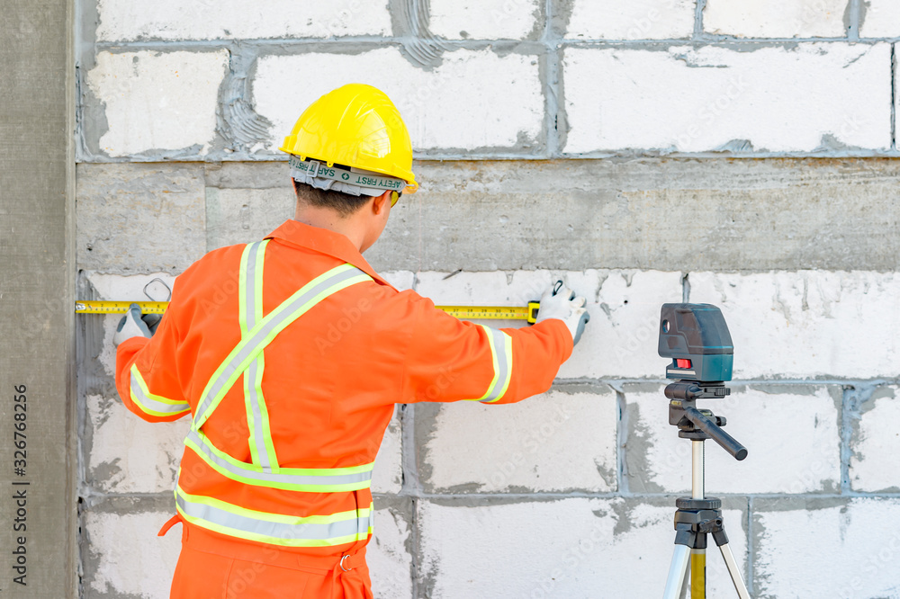 Poster construction workers is using a laser level meter for wall leveling device