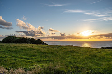 Golden sunse scene with green grass hills and ocean behind at Chiloe Island, Chile