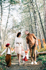 happy family of four in the middle of a pine forest in the autumn, colorful foliage on the trees