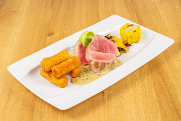 Beautiful pork tenderloin with fried potato dumplings on white rectangular ceramic plate on lacquered wood