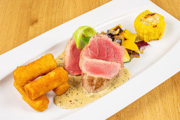 Beautiful pork tenderloin with fried potato dumplings on white rectangular ceramic plate on lacquered wood