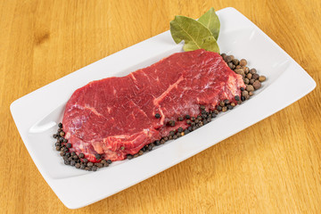 Beautiful raw beef sirloin with spices on white rectangular ceramic plate on lacquered wood