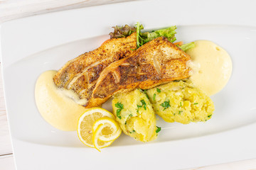 Beautiful zander with smashed potatoes on white rectangular ceramic plate flatlay on white wood