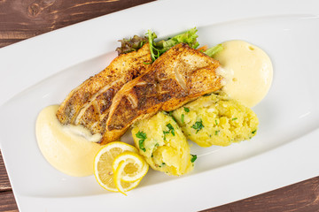 Beautiful zander with smashed potatoes on white rectangular ceramic plate flatlay on brown wood