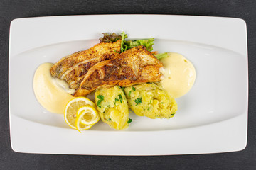 Beautiful zander with smashed potatoes on white rectangular ceramic plate flatlay on grey stone
