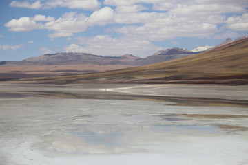 Bolivia highlands, Andes. Lake with calm waters, mountains in the background, blue sky with white clouds, 