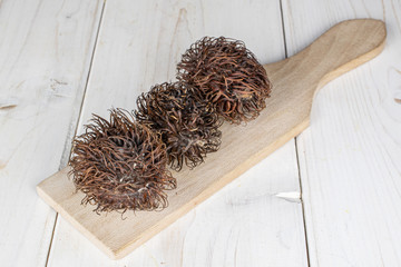 Group of three whole old brown rambutan on wooden cutting board on white wood