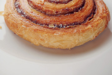 One crispy cinnamon roll on a white plate, bakery product. Close up.