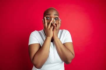 Scared crazy. African-american young woman's portrait on red background. Beautiful female model in shirt. Concept of human emotions, facial expression, sales, ad, inclusion, diversity. Copyspace.