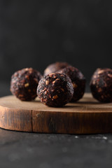 Raw vegan snack. Homemade energy balls with green buckwheat, nuts and fruits on wooden slab on black background selective focus side view