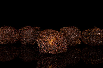 Group of five whole old brown rambutan one in focus isolated on black glass