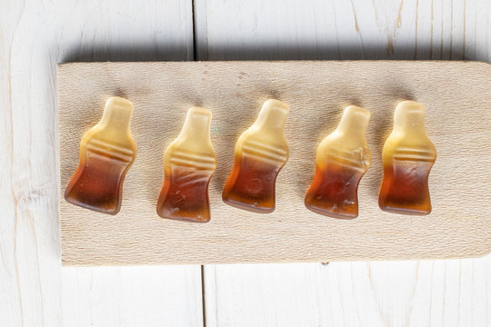 Group Of Five Whole Sweet Jelly Cola On Wooden Cutting Board Flatlay On White Wood