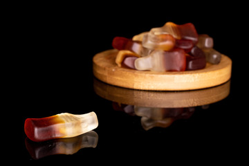 Lot of whole sweet jelly cola on round bamboo coaster isolated on black glass