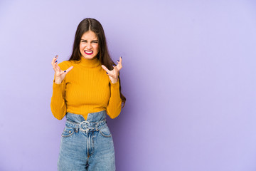 Young caucasian woman isolated on purple background upset screaming with tense hands.