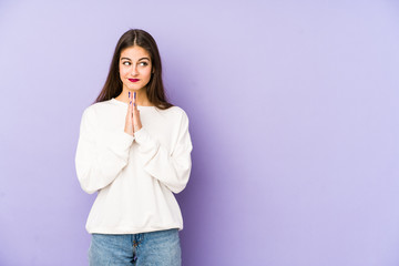 Young caucasian woman isolated on purple background praying, showing devotion, religious person...
