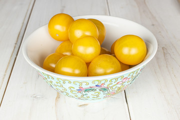 Lot of whole fresh yellow tomato with blue chinese ceramic bowl on white wood