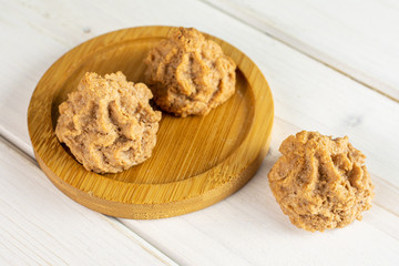 Group of three whole homemade brown coconut biscuit with chocolate on bamboo coaster on white wood