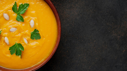 Pumpkin cream soup with seeds and herbs on a stone background, with copy space for your text. Healthy food.
