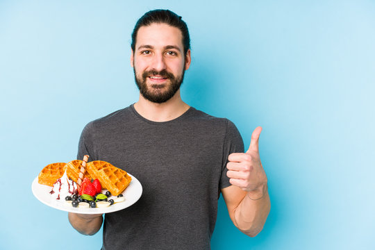 Young Caucasian Man Eating A Waffle Dessert Isolated Smiling And Raising Thumb Up