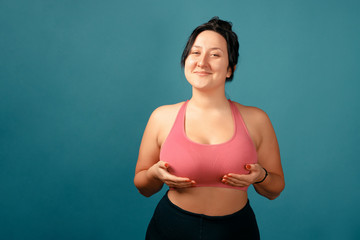 Fototapeta na wymiar Happy plus size positive woman. Happy body positive concept. I love my body. Attractive overweight woman posing on camera in the studio on a colored background. Girl demonstrates her natural bubs.