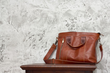 Fototapeta na wymiar Leather business bag and accessories in the work room with gray concrete wall, wood table and leather chair.