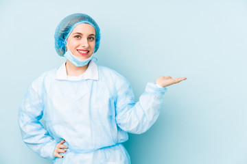 Young surgeon woman isolated showing a copy space on a palm and holding another hand on waist.