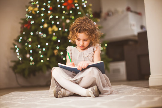 Preschool girl sitting next to festive tree and drawing