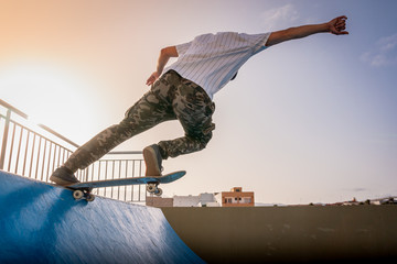 joven skater toca el borde de la rampa con su tabla al atardecer - obrazy, fototapety, plakaty