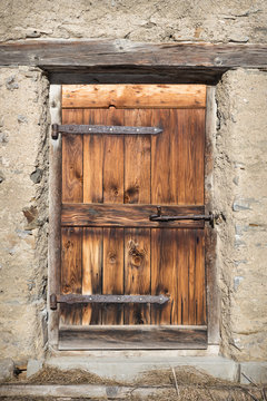 Closed old wooden door of alpine cabin or alpine hut surrounded by rustic natural stone wall.