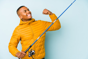 Young fisherman man isolated on a blue background raising fist after a victory, winner concept.