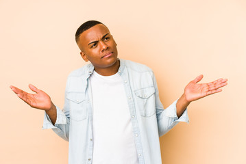 Young latin man isolated on beige background doubting and shrugging shoulders in questioning gesture.