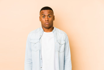 Young latin man isolated on beige background shrugs shoulders and open eyes confused.