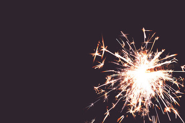 Fototapeta premium closeup view on burning sparkler in front of hazy toned black background - copy space for text