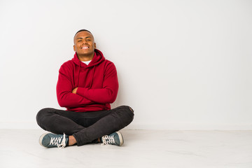 Young latin man sitting on the floor isolated laughing and having fun.