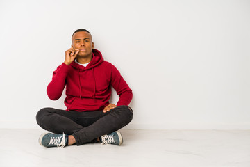 Young latin man sitting on the floor isolated with fingers on lips keeping a secret.