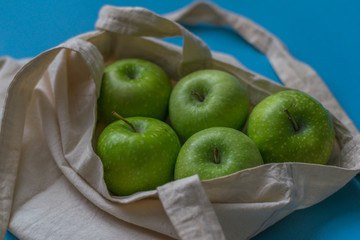 Eco friendly friend's bag for linen products with beautiful green apples on a blue background against a plastic bag.