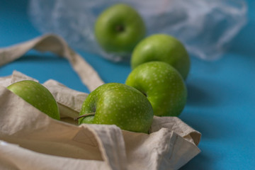 Eco friendly friend's bag for linen products with beautiful green apples on a blue background against a plastic bag.
