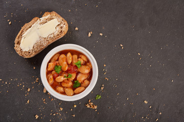 Baked beans in tomato sauce on black stoneware with bread, meal.