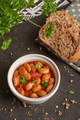 Baked beans in tomato sauce on black stoneware with bread, meal.