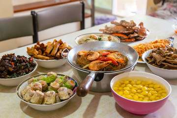 Casseroled prawns with Glass Noodels in Small Iron Pan with Fish, Fried Spring Rolls, Dim Sum, Seafood, Roasted Duck and Meatball Background on the Table.