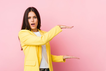 Young business woman shocked and amazed holding a copy space between hands.