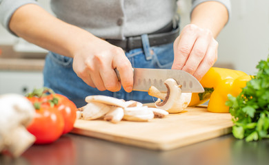 Woman is cutting mushroom on kitchen table.