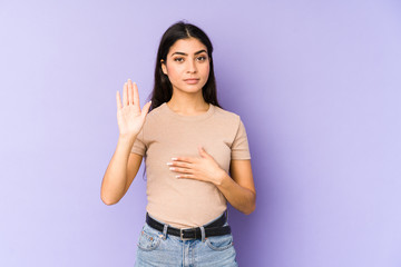 Young indian woman isolated on purple background taking an oath, putting hand on chest.