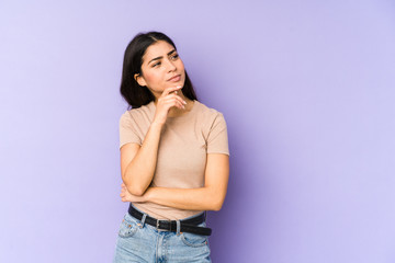 Young indian woman isolated on purple background looking sideways with doubtful and skeptical expression.