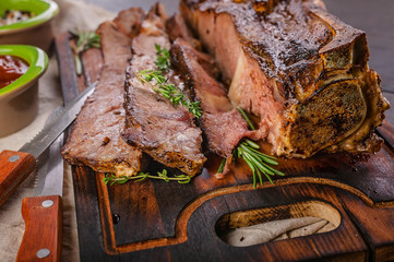 Close-up beef steak on the bone with spices and sauce on a wooden cutting board.